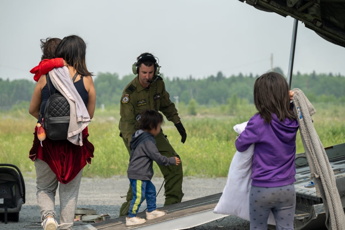 A Canadian Armed Forces member helps a child onto an aircraft.