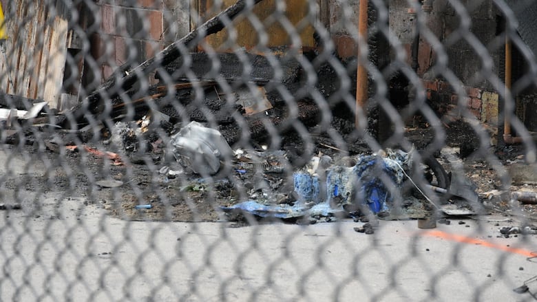Blackened debris next to a brick wall shot through a fence. 