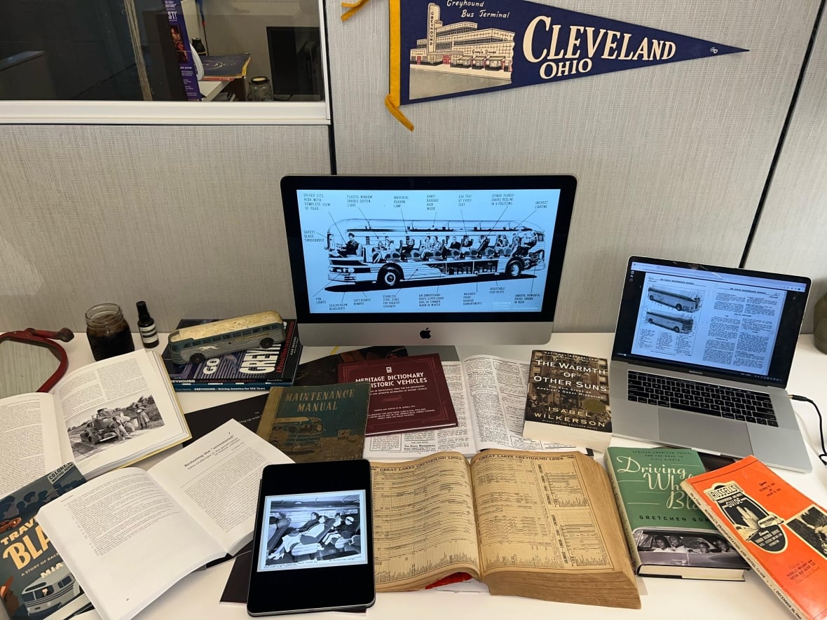 A desk covered in books, with a computer monitor showing a screen with a bus diagram on it.