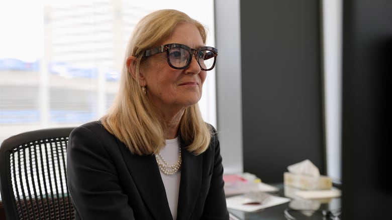 A woman looks at a computer screen while sitting at a desk. The woman is wearing a white shirt and a black blazer.