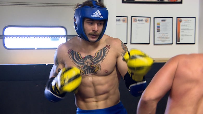 A man in a helmet and boxing gloves spars with an opponent in a gym.