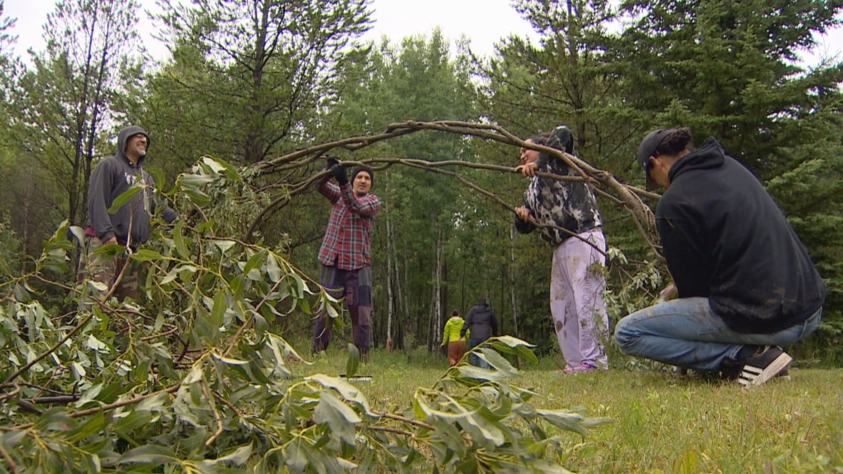 A group of people hold willow branches in a clearing surrounded by trees.