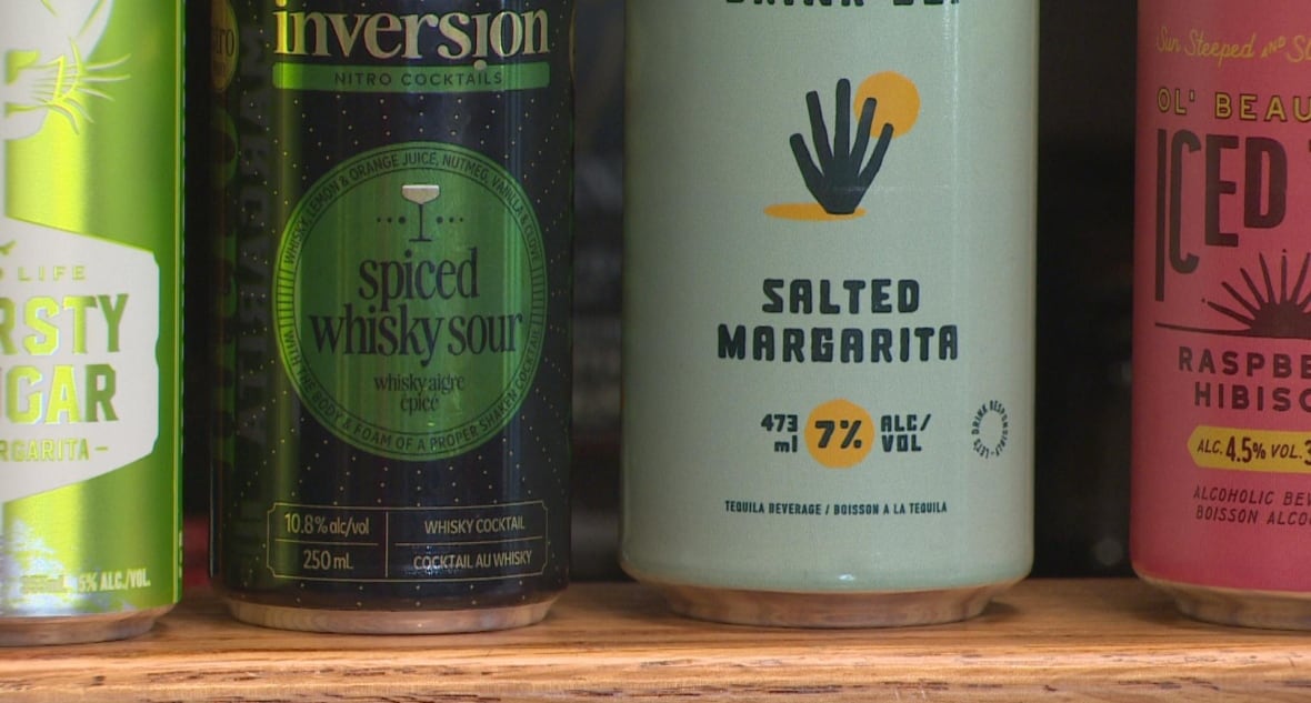 a green can, a black can, a light blue can and a pink can of alcohol sit next to eachother on a wooden shelf