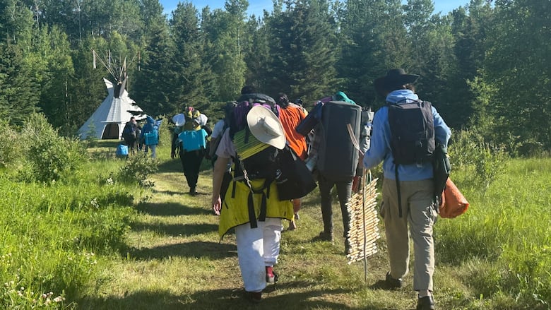 A group of people walk on a grass path toward a teepee.