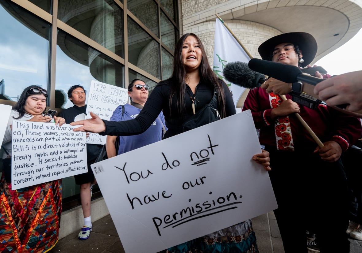 A young woman stands holding a sign that says: You do not have our permission.