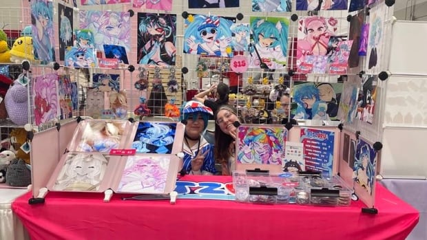 Women seated at a pink booth selling art.