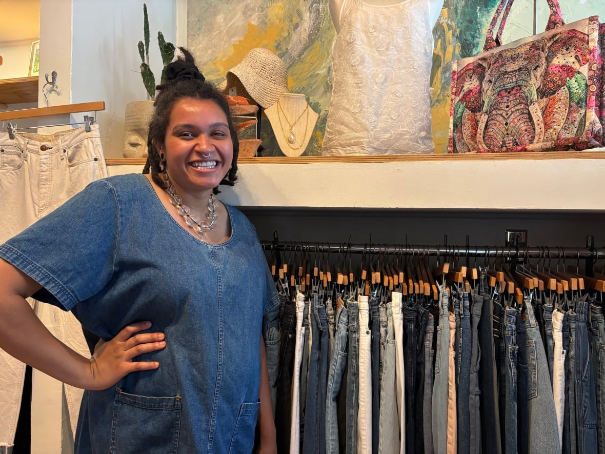 A woman stands next to a rack of clothing, smiling at the camera.