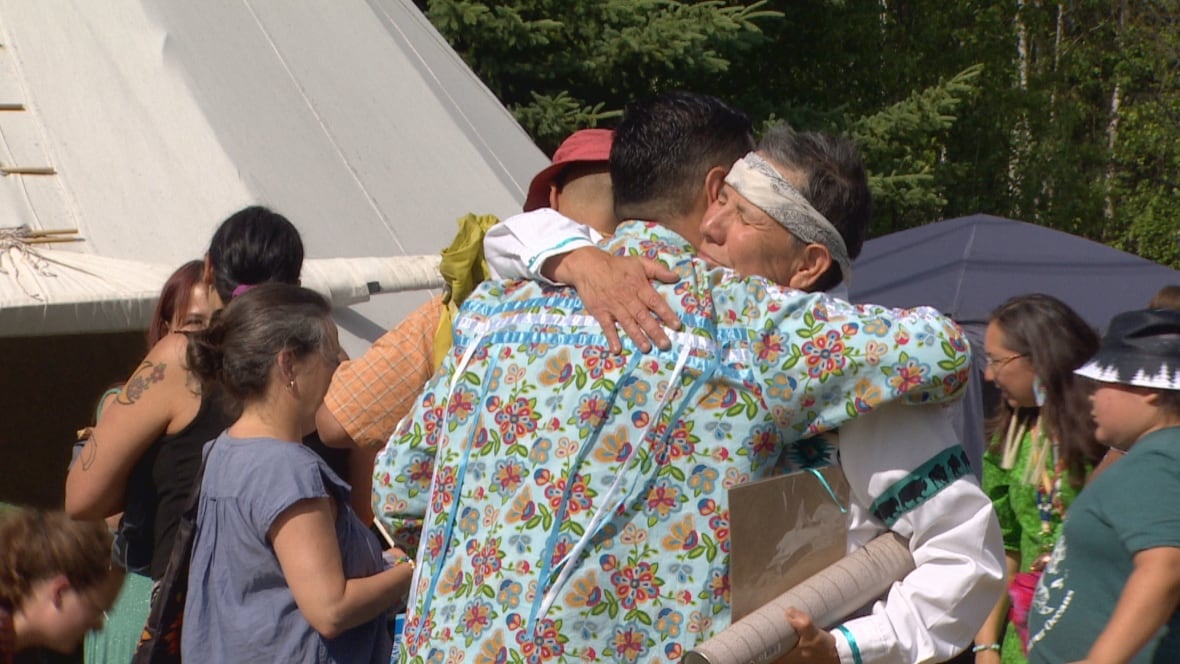 Two people hugging. Other people are visible in the background.