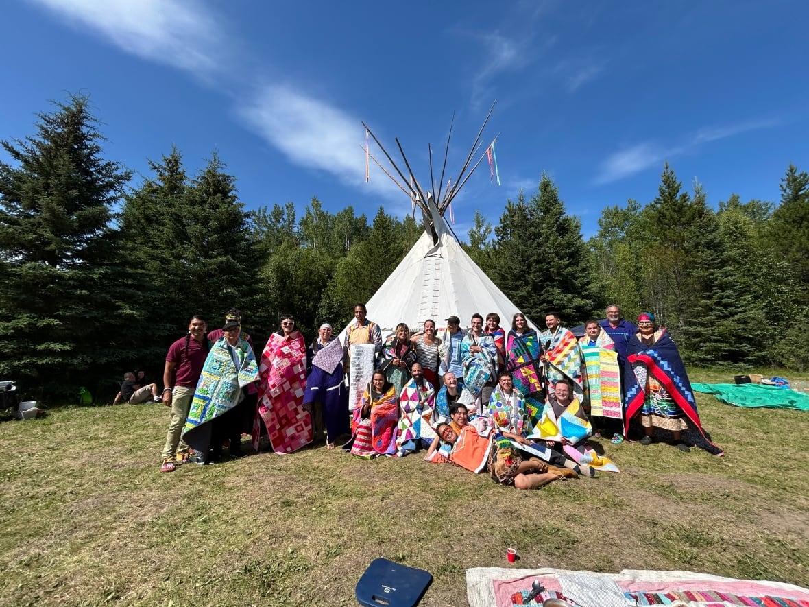 A group of people pose for a photo in front of a teepee.