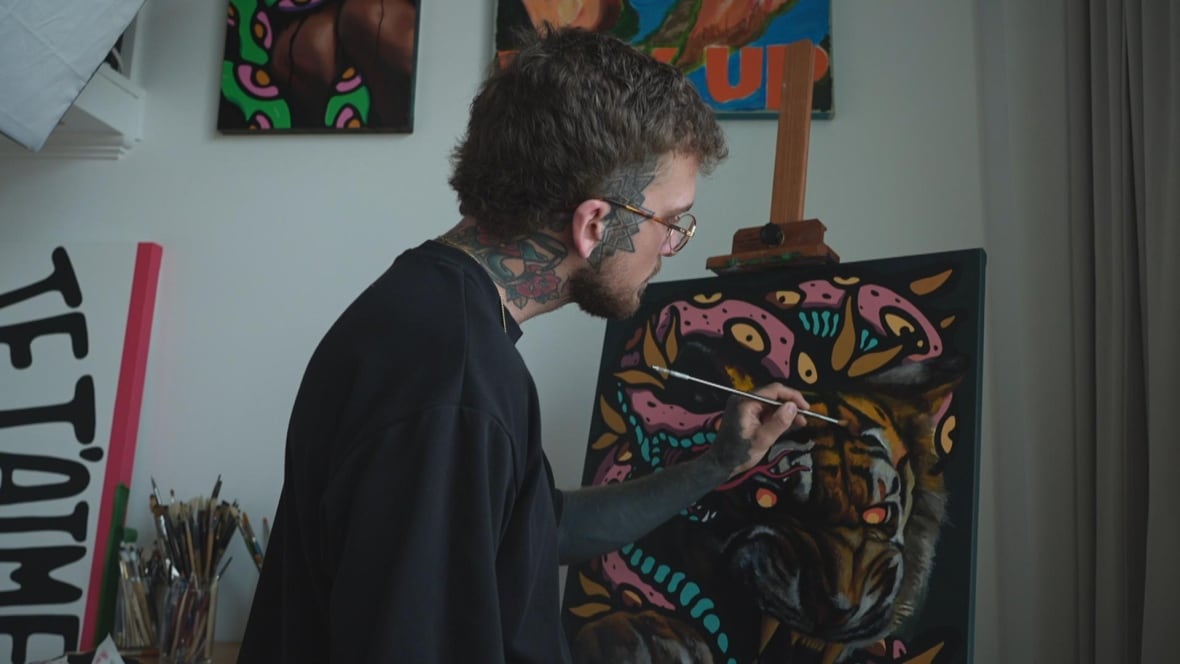 Tattooed man painting a canvas with a tiger and a snake on it