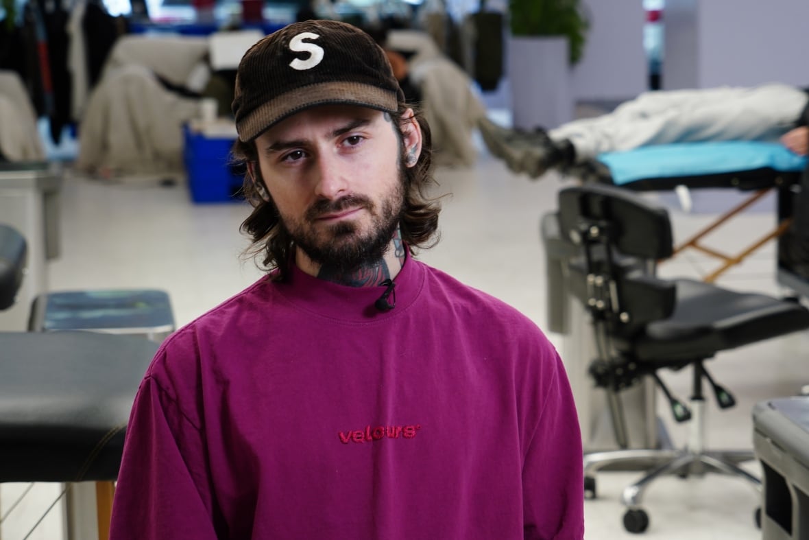 A man with tattoos, a purple shirt and a baseball cap in a tattoo parlour