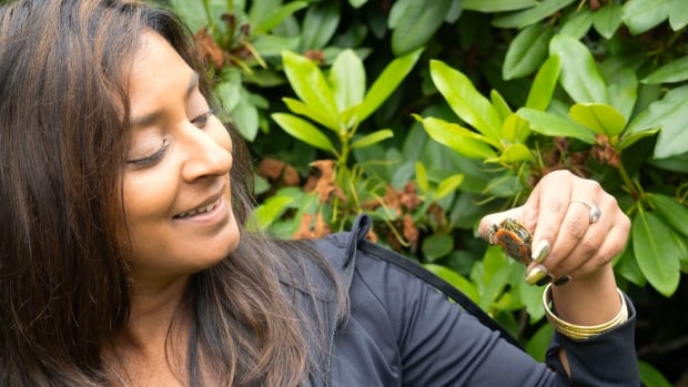 A woman holds a small turtle in her hand and smiles at it.