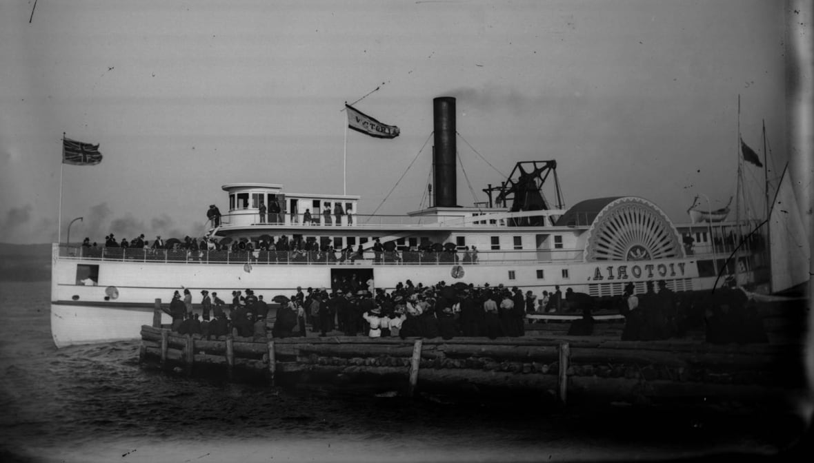 A black and white picture of a steamboat at a wharf picking up passengers.