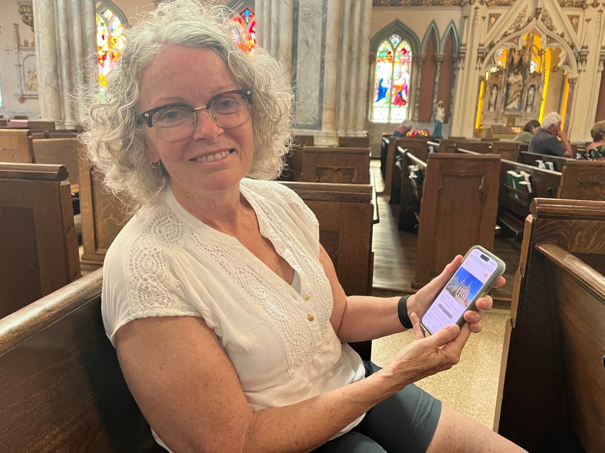 A woman sits in a church pew, holding her phone.
