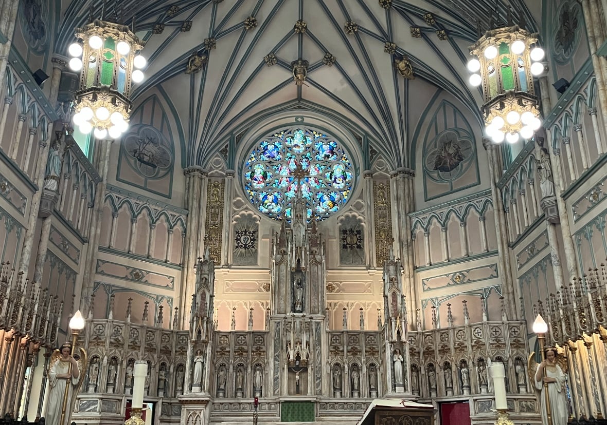 A rose stained glass window is framed by connecting ribs from the vaulted ceiling.