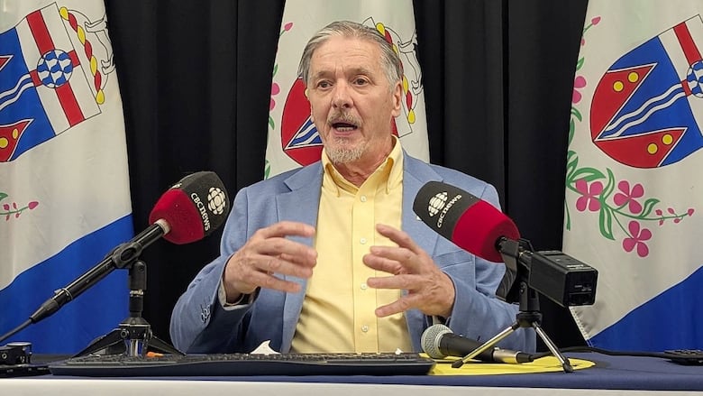 A man in a shirt and blazer gestures with his hands while speaking at a news conference.