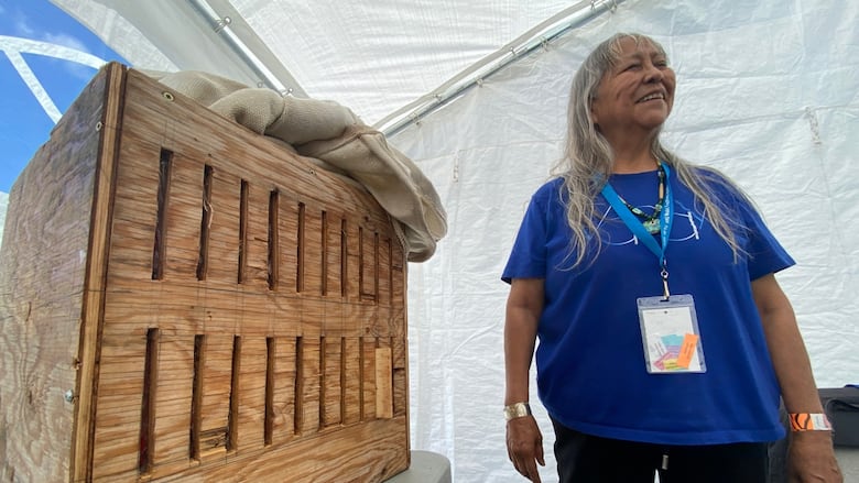 A smiling woman stands near a wooden box.