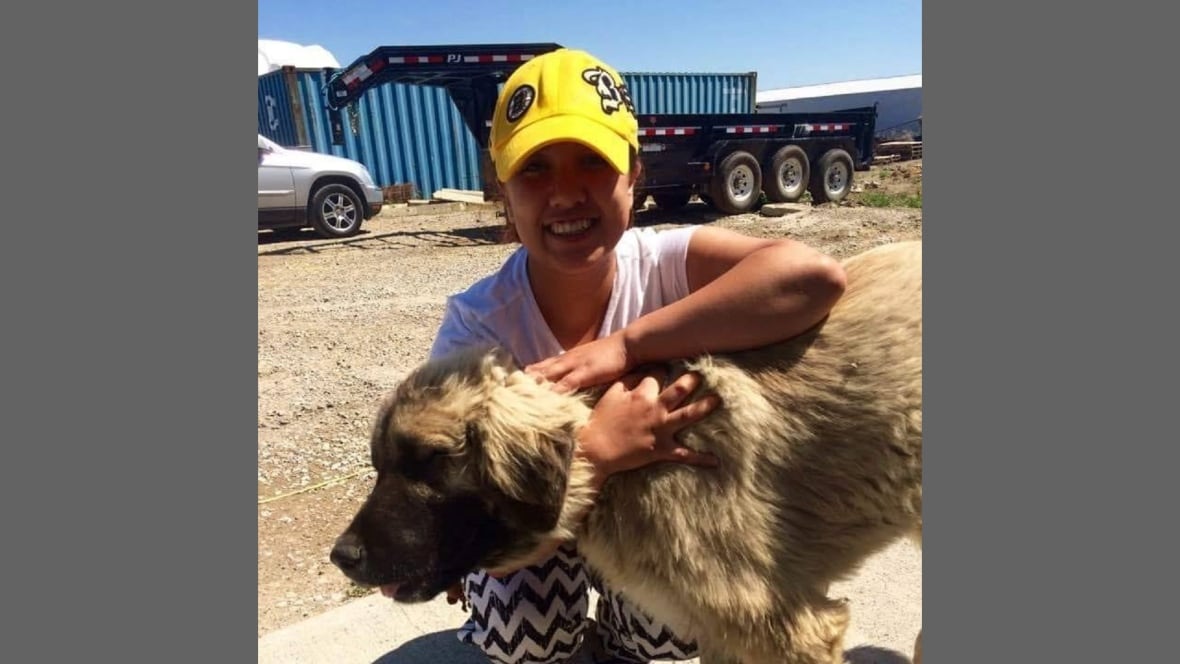 A smiling woman holds a dog at an outdoor work site.