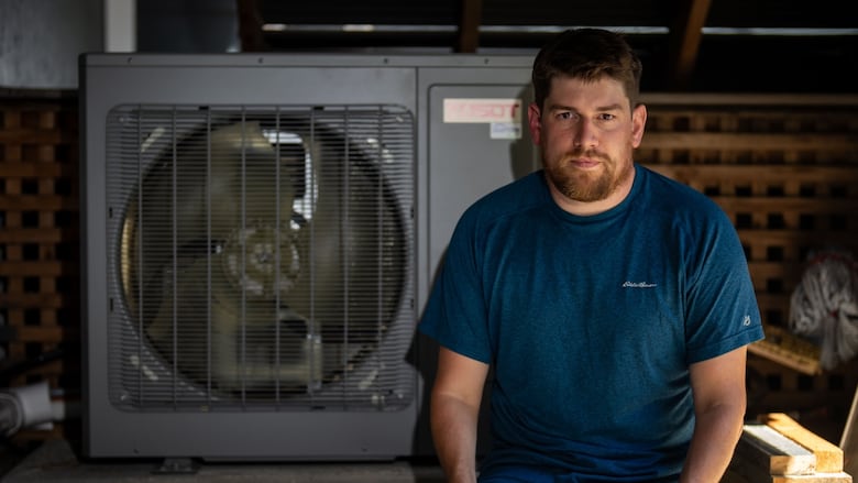 A man sits in front of a large fan, the cooling unit for a heat pump.