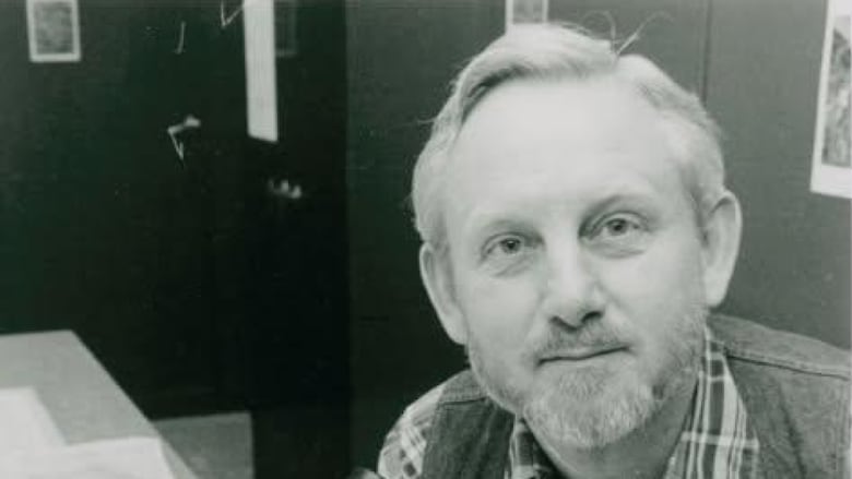 A black and white photo of a man with short hair before a microscope.
