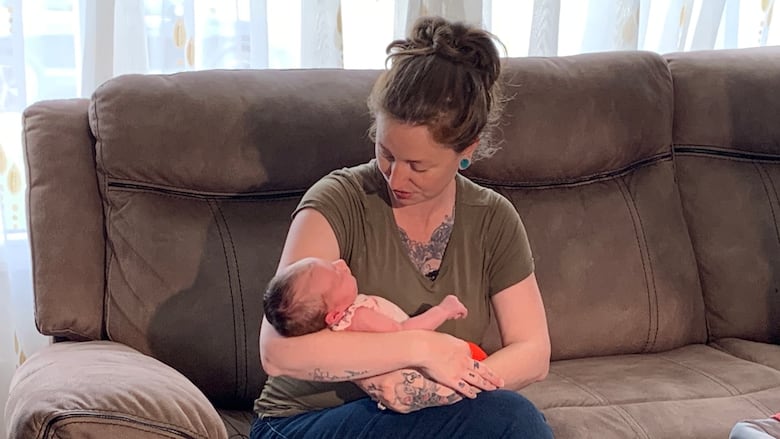 A woman in a green shirt holds a newborn baby.