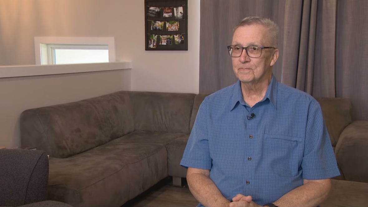 A man in a blue shirt sits in a living room.