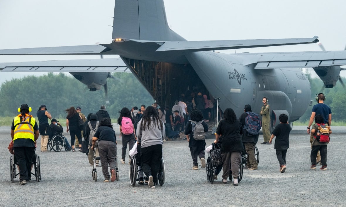 People approach the open rear end of an aircraft, many in wheelchairs. Some people can be seen already inside the plane.