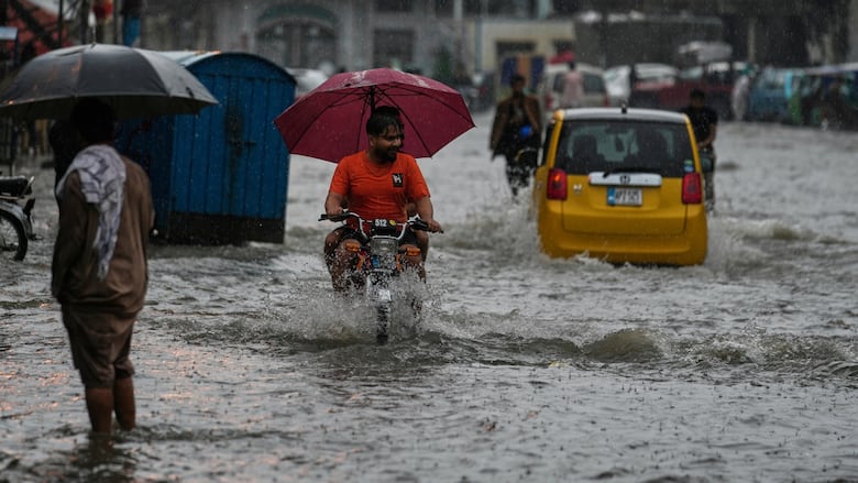 Motorists and pedestrians make their way through shin-deep water in a heavily flooded street.