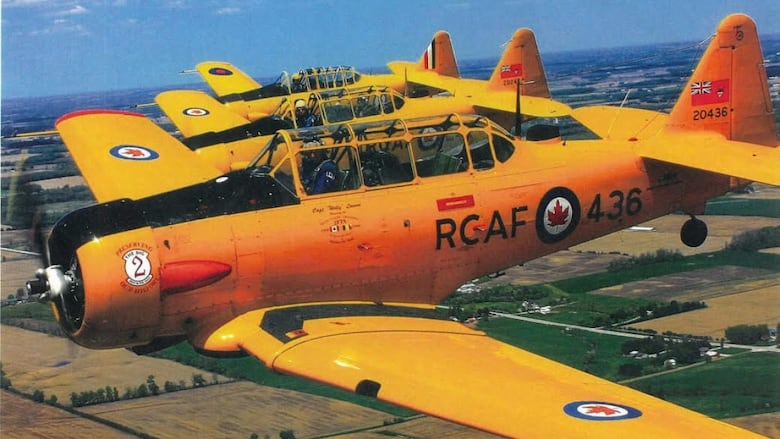A yellow plane flies above green fields.