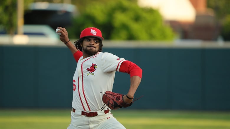 A man wearing a red and white baseball uniform holds his breath as he throws a pitch