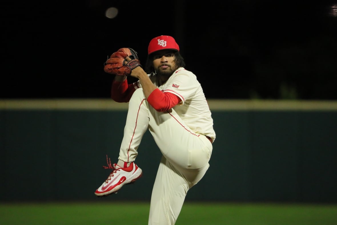 A man lifts his leg and stares at the camera as he prepares to throw a pitch.