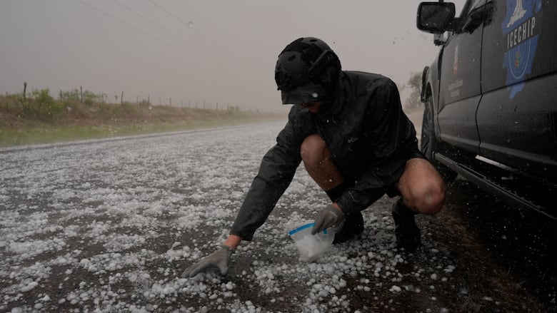 A person scoops up hail on a road.