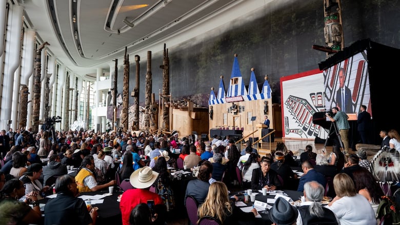 A wide shot of Indigenous leaders listening while Prime Minister Carney speaks at a podium.