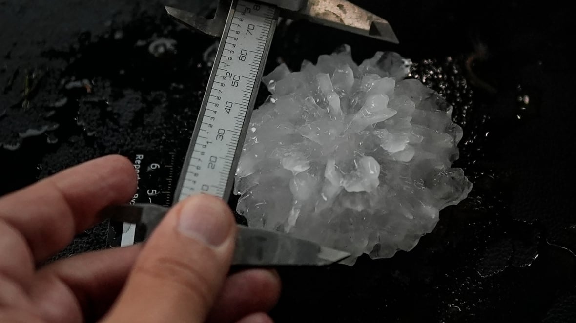 A hand is seen measuring a piece of hail.