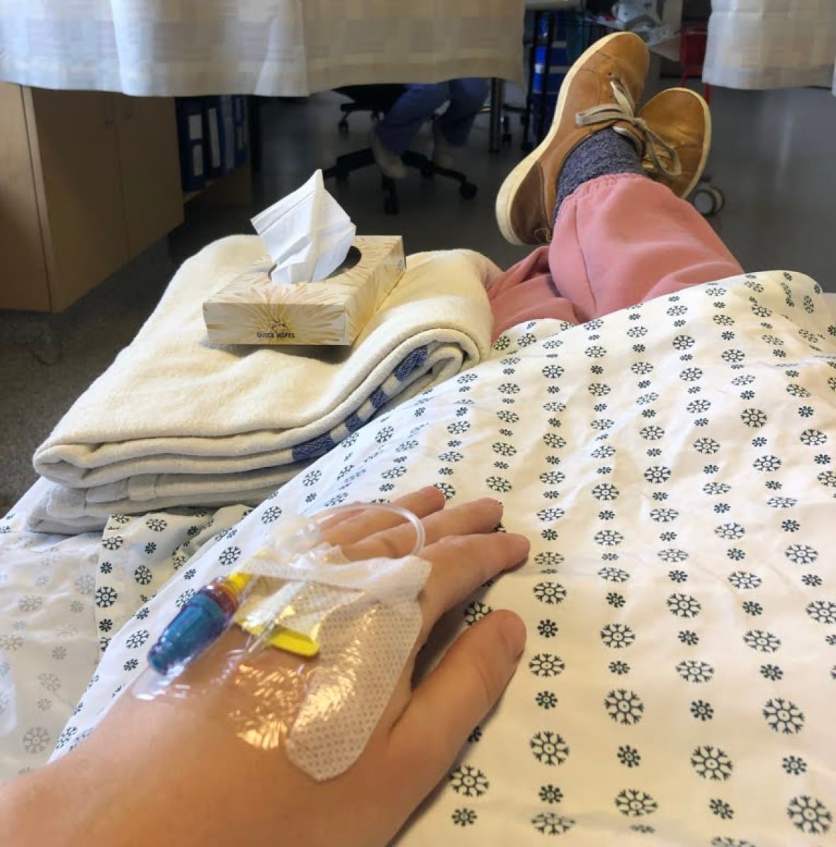 Brinn Edgington sentada y acostada en una cama de hospital, con una bata. Tiene tubos conectados a su mano izquierda.