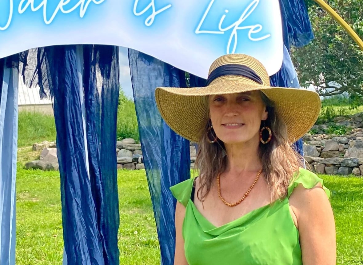 Photo of a woman in front of a sign that reads "Water is life."