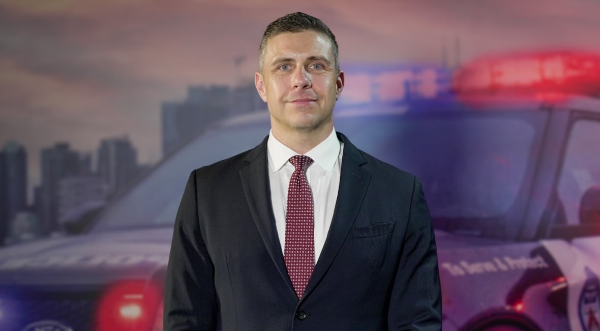 Man in a suit standing in front of a mural of a police car.