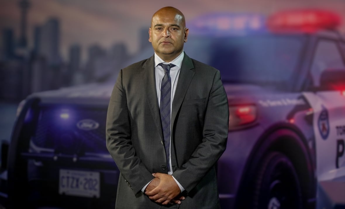 Man in a suit standing in front of a mural of a police cruiser.