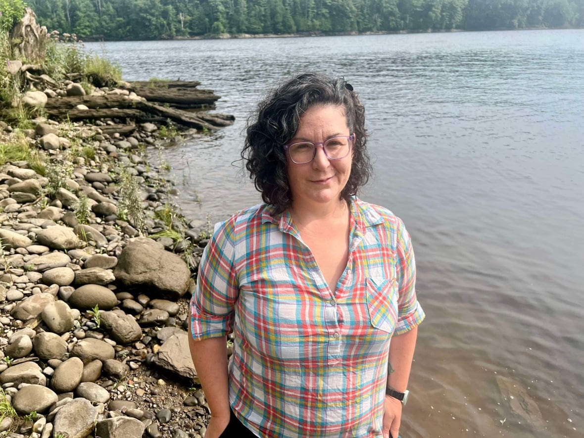 Woman with dark hair and glasses standing next to water.