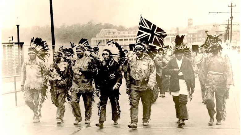 Black and white photo of Indigenous people crossing bridge holding flags.