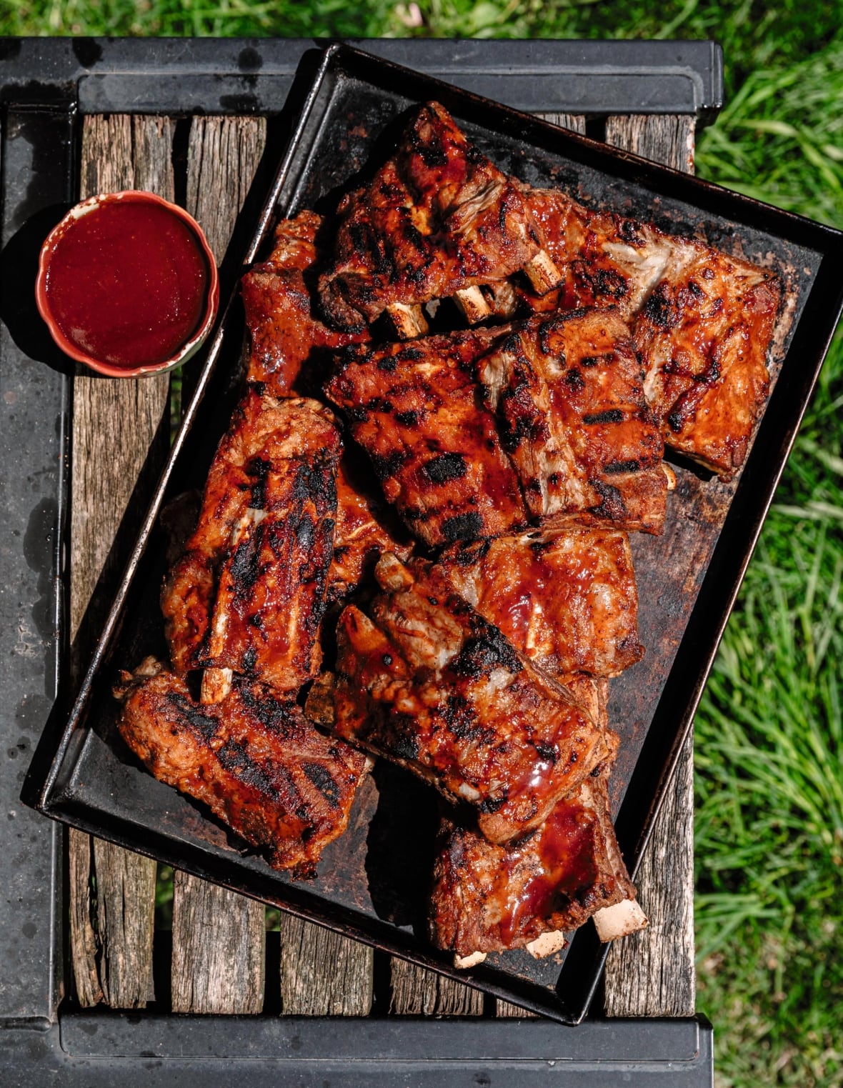 Top down shot of barbecued ribs on the side of a barbecue with grass in the background.