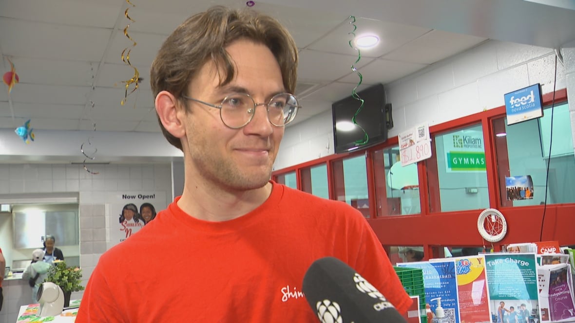 A man in a red YMCA t-shirt speaks into a microphone.