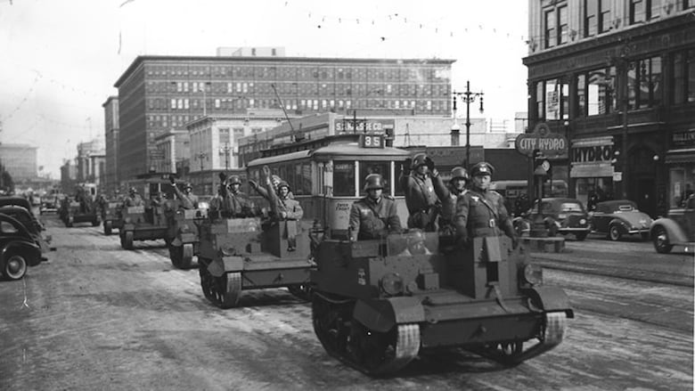 A black and white photo shows tanks with men dressed in Nazi uniforms. 