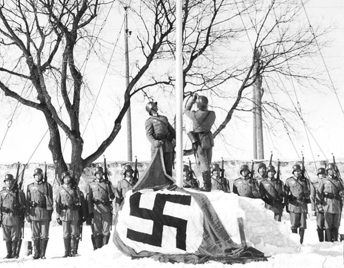A black and white photo with men in uniform raising a flag.