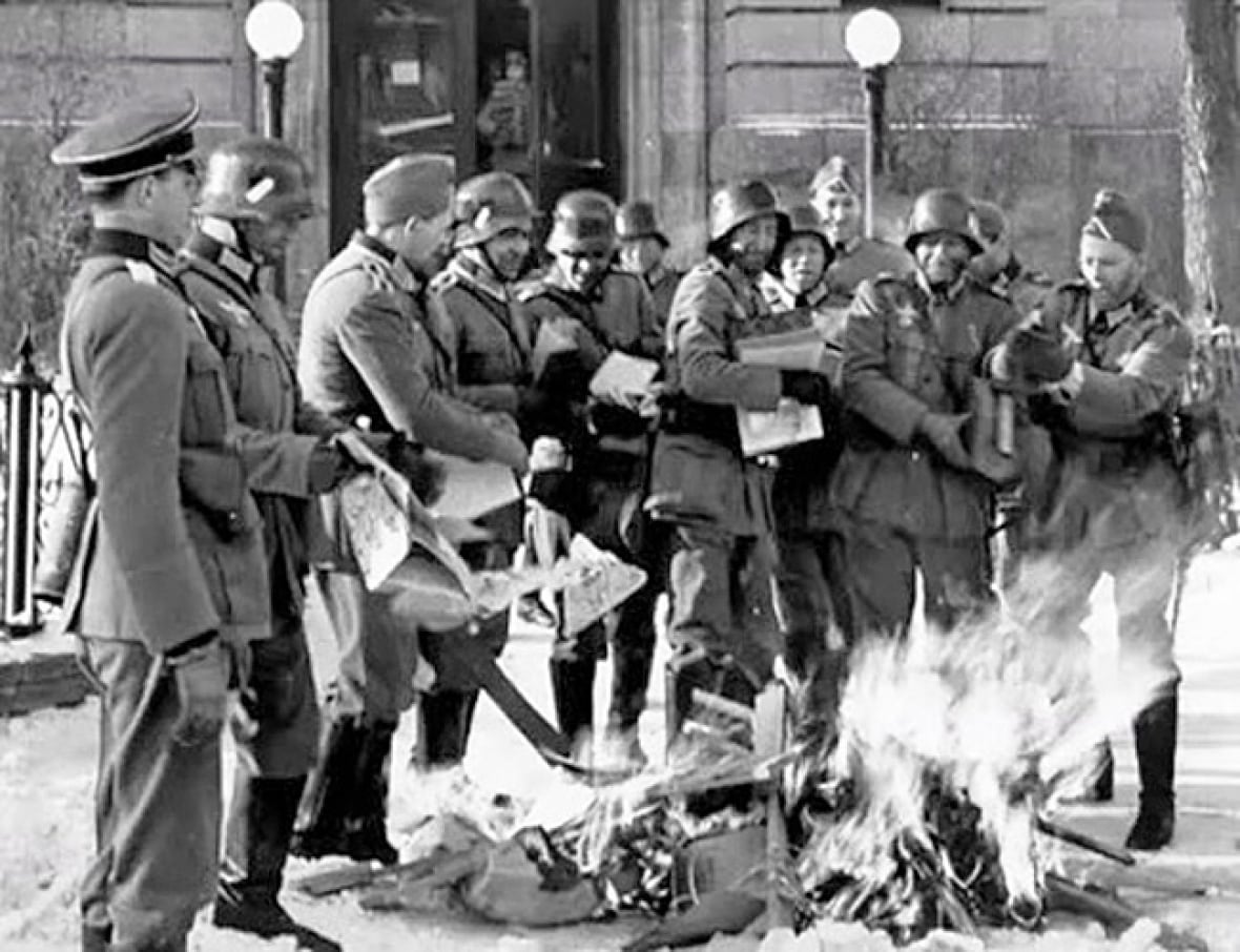 A black and white image shows men in army uniforms burning books.