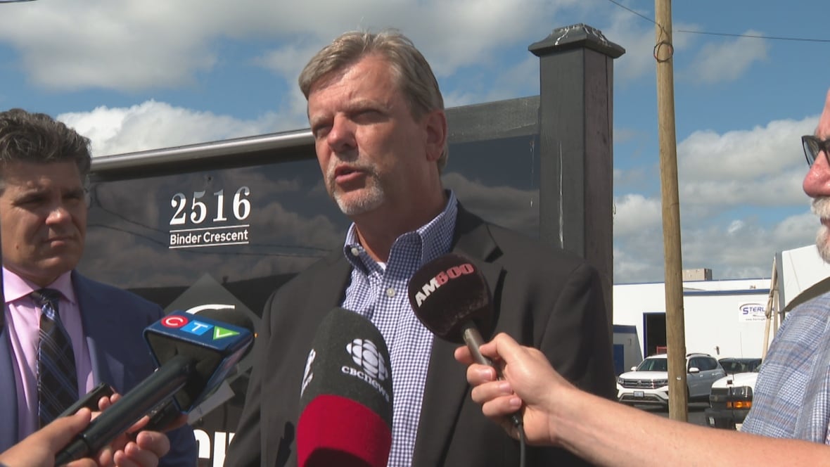 Close-up of Ron outdoors on a very sunny day with several microphones pointed at his mouth. 