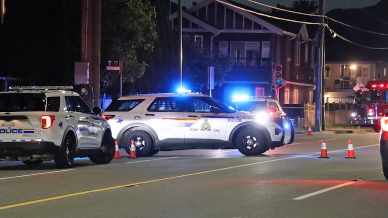 Three RCMP police cruisers with flashing lights at various angles on a city road.