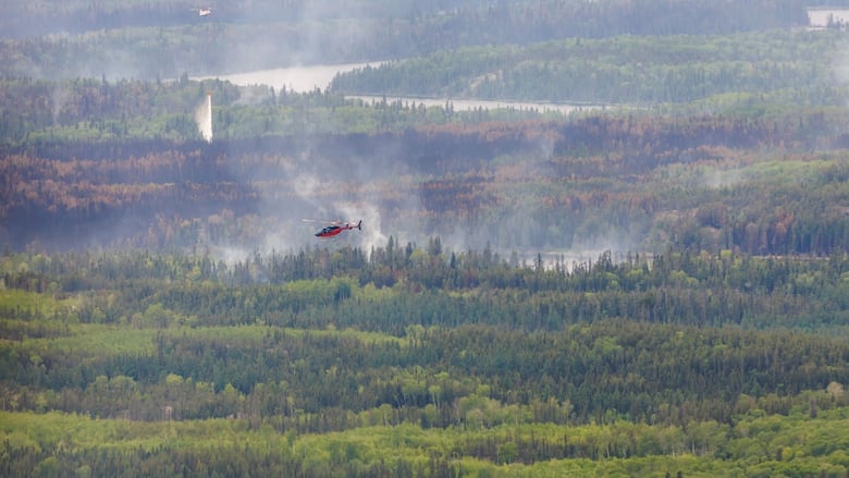 A helicopter crew works on a wildfire as another is shown flying by in northern Manitoba during a helicopter tour in the surrounding area of Flin Flon, Man. on Thursday, June 12, 2025.