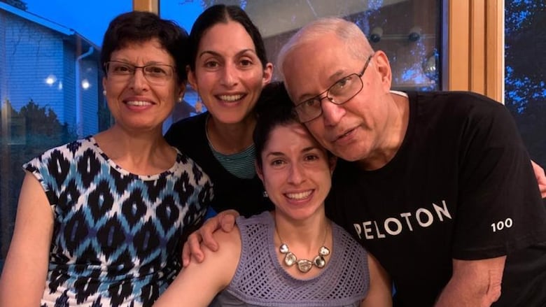Family stands and sits behind fruit cake that says "happy birthday," smiling