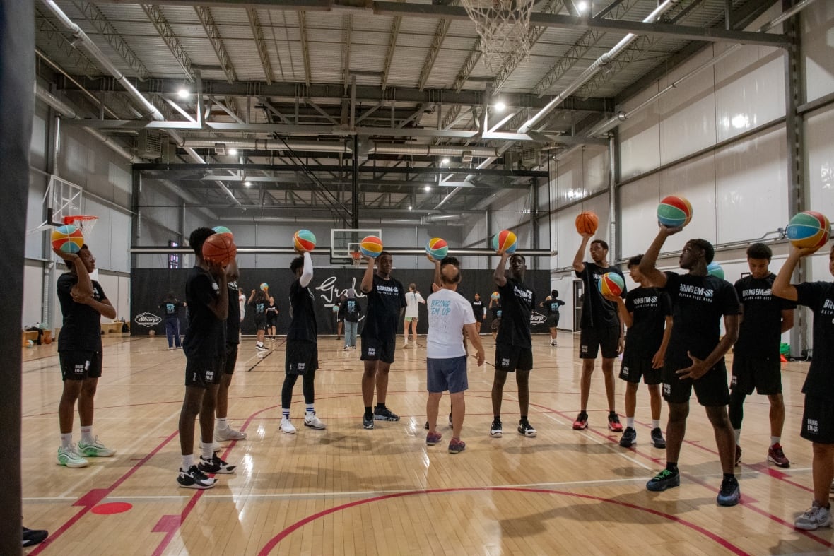 A line of kids all dressed in black hold up colourful basketballs.